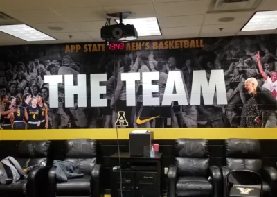 Lounge mural for App State Men's Basketball. "The Team" is printed large across the wall with a collage of game photographs. Below the text is the App State Mountaineers logo and the Nike Check.