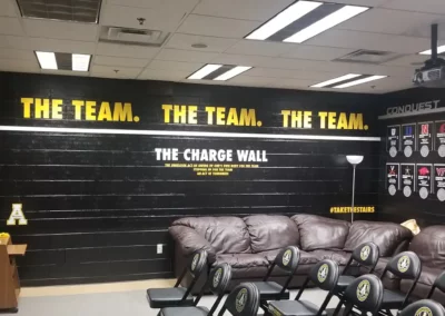 Wall mural with text that reads "The Team" in all caps. Below reads "The Charge Wall: The unselfish act of giving up one's own body for the team stepping up for the team an act of toughness" and "#takethestairs".