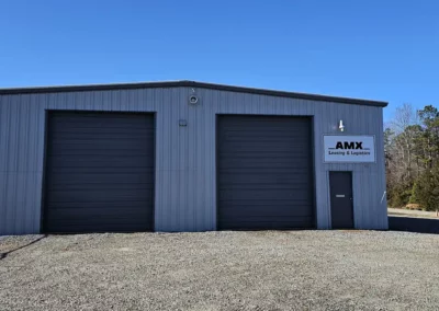 Logo with wordmark printed on a large sign hanging over a workshop door. Logo icon is big bold text reading "AMX". Below is the tagline reading "Leasing & Logistics".