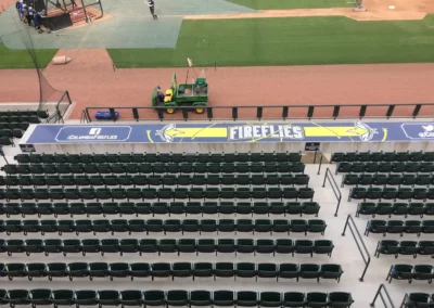 Baseball stadium seating facing a large horizontal banner with the Columbia Fireflies logo. Also printed is the Facebook link "facebook.com/columbiafireflies".