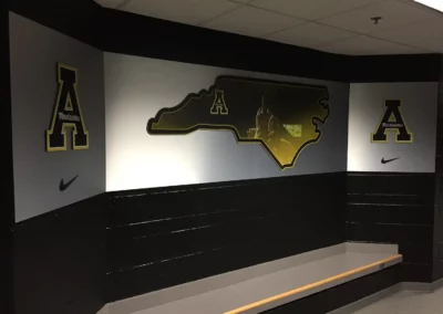 Wall branding mountain ion metal sheets. Displays the App State Mountaineers logo with a large image of NC state in the middle. The state has an image inside it of hands raised in the air.