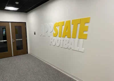 Office wall fixture for Appalachian State University Football. Text in white and yellow reads "App State Football". Presented in large but thin cut-outs of letters that just barely protrude from the wall.