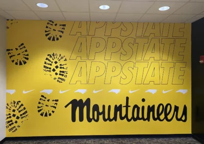 Office wall mural for Appalachian state University. Full yellow background with large boot prints spanning the left side. Text spanning the right side reads "App State Mountaineers".